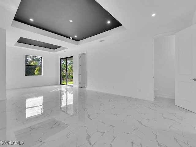 empty room with a tray ceiling, recessed lighting, and marble finish floor