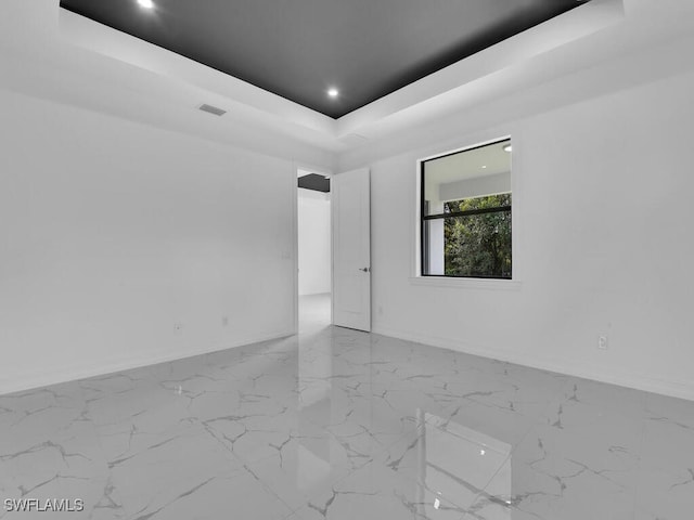 empty room with recessed lighting, marble finish floor, baseboards, and a tray ceiling