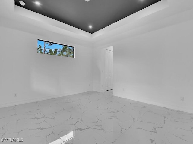 unfurnished room with recessed lighting, marble finish floor, a raised ceiling, and baseboards