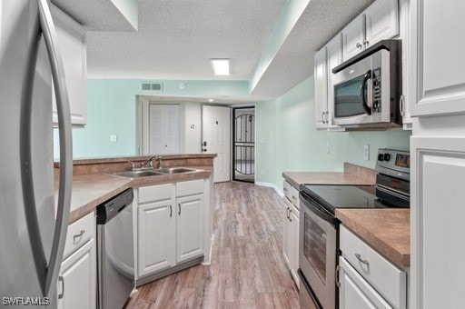 kitchen with sink, stainless steel appliances, a textured ceiling, white cabinets, and light wood-type flooring