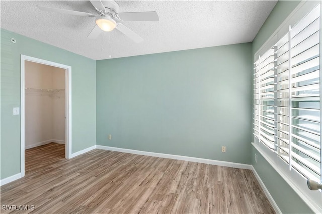 unfurnished bedroom featuring light hardwood / wood-style flooring, ceiling fan, a spacious closet, a textured ceiling, and a closet