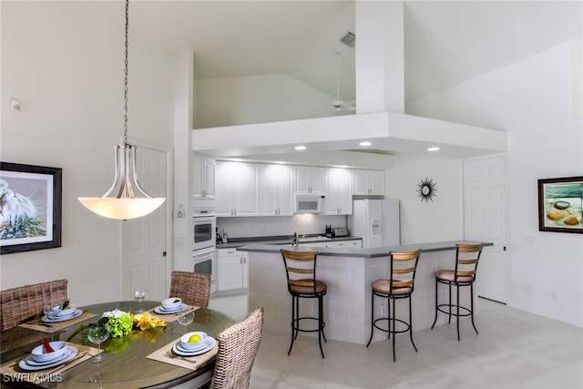 kitchen with a kitchen breakfast bar, white appliances, decorative light fixtures, high vaulted ceiling, and white cabinetry