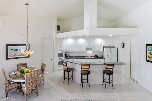 kitchen featuring a breakfast bar, white appliances, high vaulted ceiling, decorative light fixtures, and white cabinetry