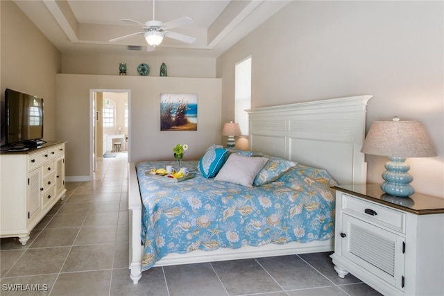 tiled bedroom featuring a tray ceiling, ensuite bath, and ceiling fan