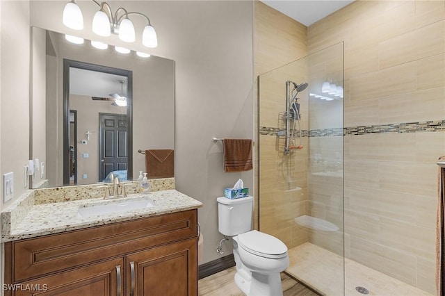 bathroom featuring ceiling fan, toilet, vanity, and a tile shower