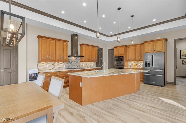 kitchen featuring light stone countertops, appliances with stainless steel finishes, a kitchen island with sink, pendant lighting, and wall chimney exhaust hood