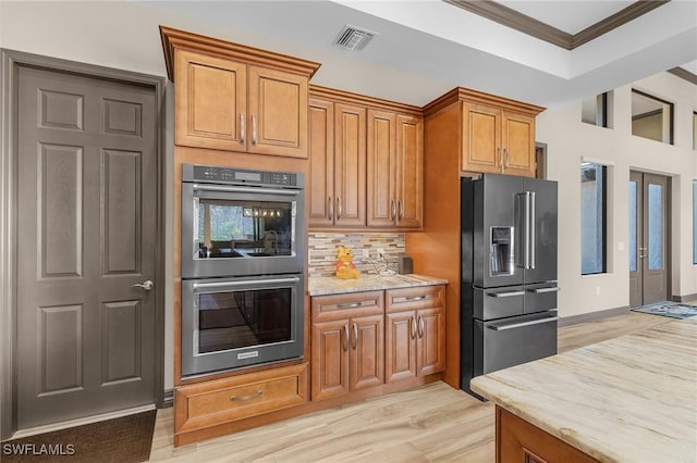 kitchen featuring light stone countertops, high end fridge, light wood-type flooring, ornamental molding, and double oven