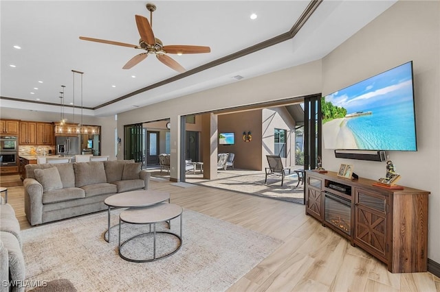 living room with ceiling fan, a tray ceiling, ornamental molding, and light wood-type flooring