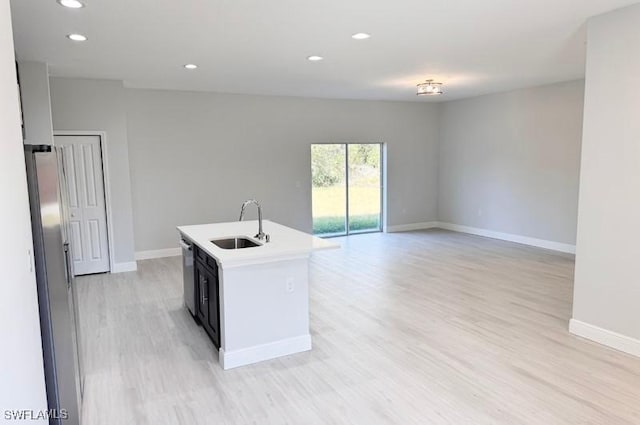 kitchen with light wood-type flooring, stainless steel appliances, a kitchen island with sink, and sink