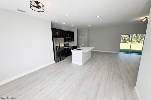 kitchen with appliances with stainless steel finishes, sink, light hardwood / wood-style floors, and an island with sink