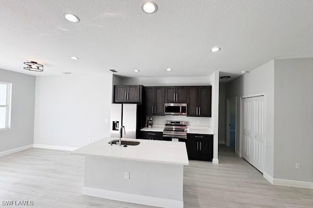 kitchen featuring sink, light hardwood / wood-style floors, a textured ceiling, a center island with sink, and appliances with stainless steel finishes