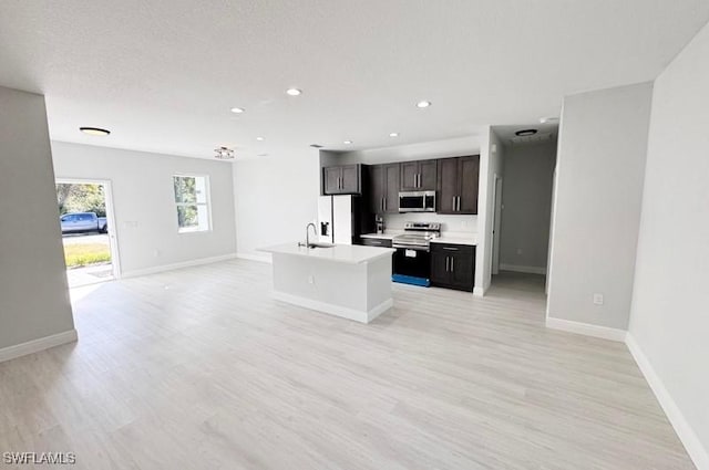 kitchen featuring stainless steel appliances, light hardwood / wood-style flooring, an island with sink, a textured ceiling, and dark brown cabinets