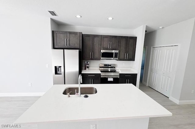 kitchen with sink, light wood-type flooring, stainless steel appliances, and a kitchen island with sink