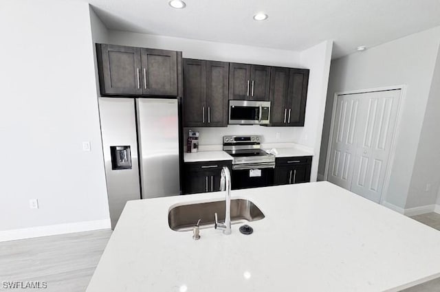 kitchen with dark brown cabinetry, stainless steel appliances, light hardwood / wood-style floors, and sink