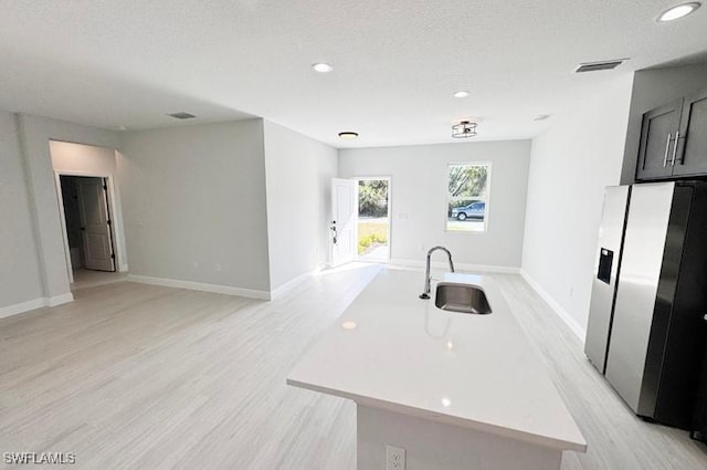 kitchen with sink, light wood-type flooring, a kitchen island with sink, and stainless steel refrigerator with ice dispenser