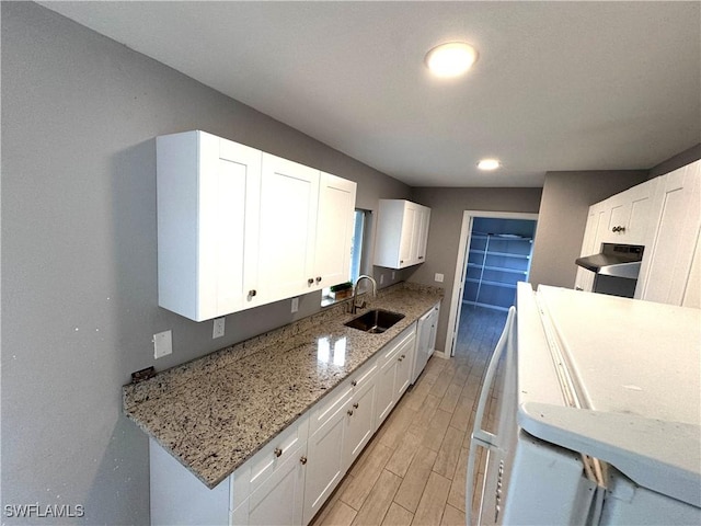 kitchen featuring white cabinetry, sink, light stone countertops, and light wood-type flooring