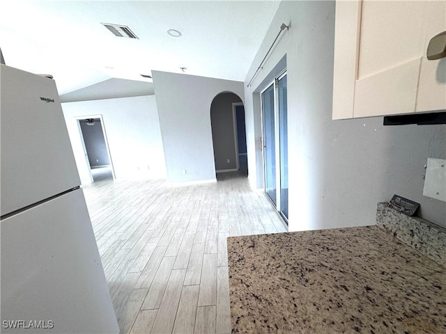 kitchen with white cabinetry, light stone counters, light hardwood / wood-style flooring, white refrigerator, and vaulted ceiling