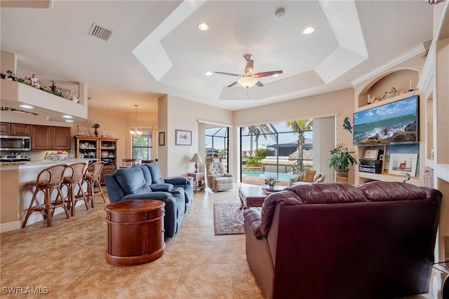 living room with ceiling fan with notable chandelier, light tile patterned floors, and a tray ceiling