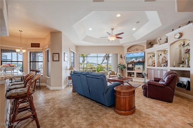 living room featuring light tile patterned floors, ceiling fan with notable chandelier, and a raised ceiling