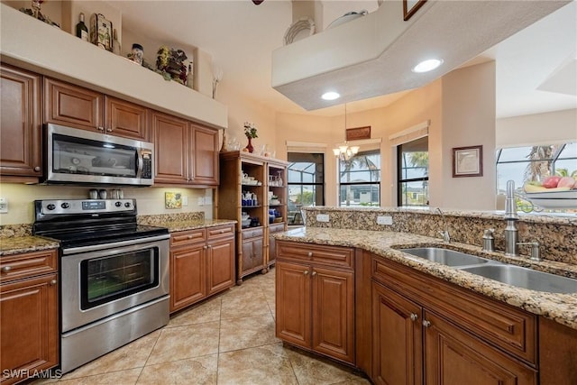 kitchen with appliances with stainless steel finishes, light stone counters, pendant lighting, a notable chandelier, and light tile patterned flooring