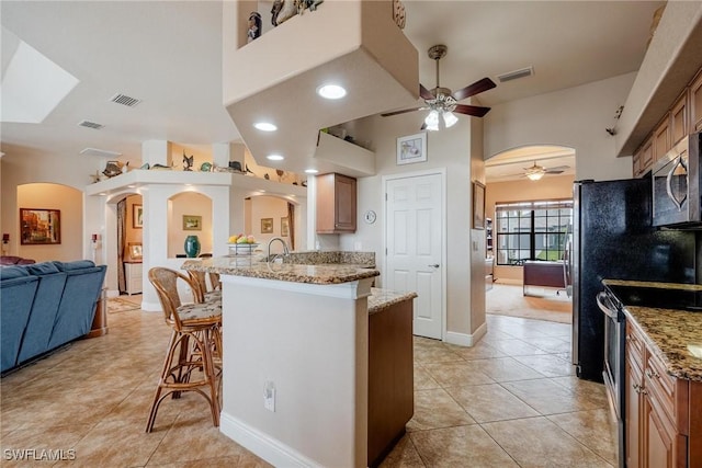 kitchen featuring a kitchen bar, light stone counters, stainless steel appliances, ceiling fan, and light tile patterned flooring