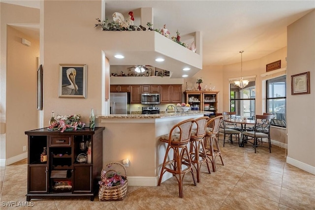 kitchen featuring a kitchen bar, appliances with stainless steel finishes, kitchen peninsula, light stone counters, and a notable chandelier