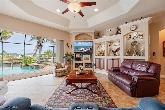 living room with ceiling fan, a raised ceiling, and light tile patterned floors