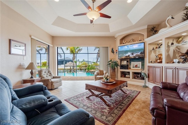 living room featuring built in features, a raised ceiling, ceiling fan, and light tile patterned flooring