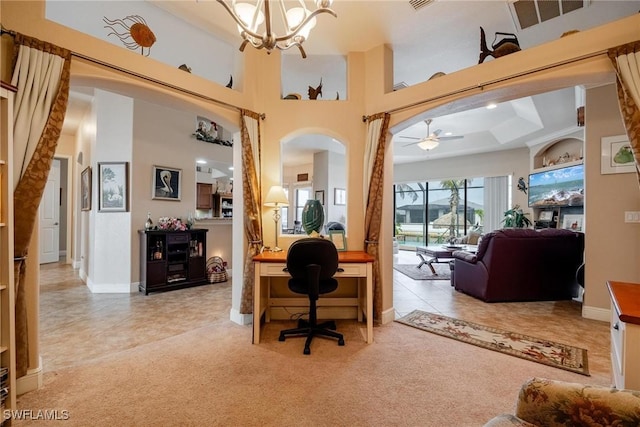 carpeted home office featuring ceiling fan with notable chandelier, a high ceiling, and a tray ceiling