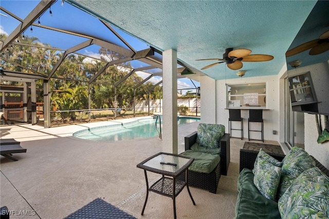 view of swimming pool featuring glass enclosure, ceiling fan, an outdoor living space, exterior bar, and a patio area