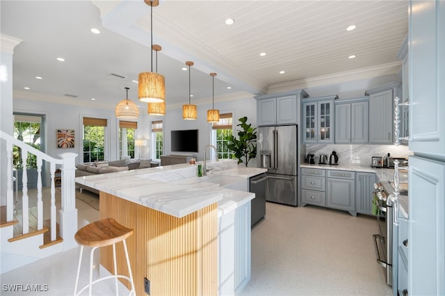 kitchen featuring a center island with sink, sink, decorative backsplash, light stone countertops, and stainless steel appliances