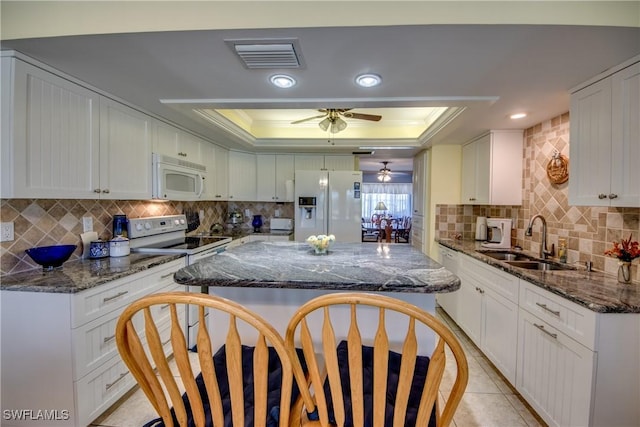 kitchen featuring white appliances, a raised ceiling, sink, dark stone countertops, and white cabinetry