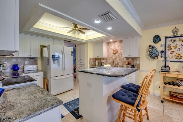 kitchen featuring ornamental molding, a tray ceiling, white refrigerator with ice dispenser, stone countertops, and white cabinetry