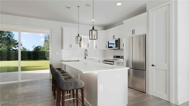 kitchen featuring a center island, sink, appliances with stainless steel finishes, decorative light fixtures, and white cabinetry