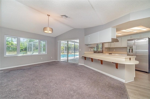 kitchen featuring white cabinetry, stainless steel fridge, vaulted ceiling, and decorative light fixtures