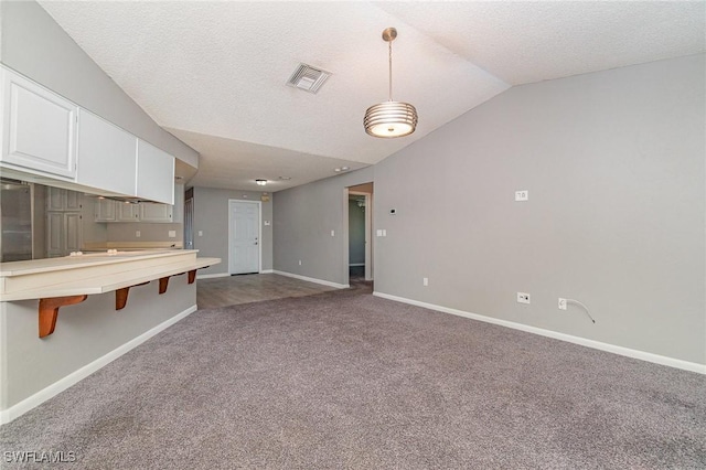 kitchen with carpet, a textured ceiling, vaulted ceiling, decorative light fixtures, and white cabinets