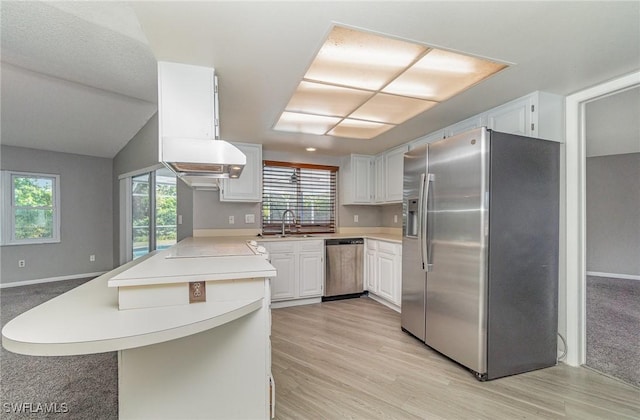 kitchen featuring kitchen peninsula, vaulted ceiling, stainless steel appliances, and white cabinetry