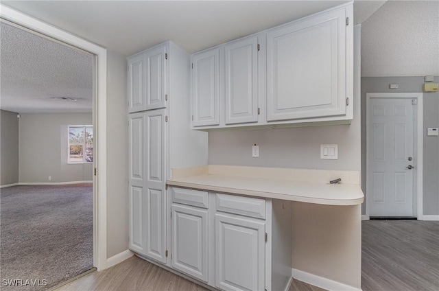 kitchen featuring a textured ceiling, light hardwood / wood-style floors, and white cabinetry