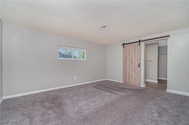 unfurnished bedroom with carpet, a barn door, a textured ceiling, and a closet