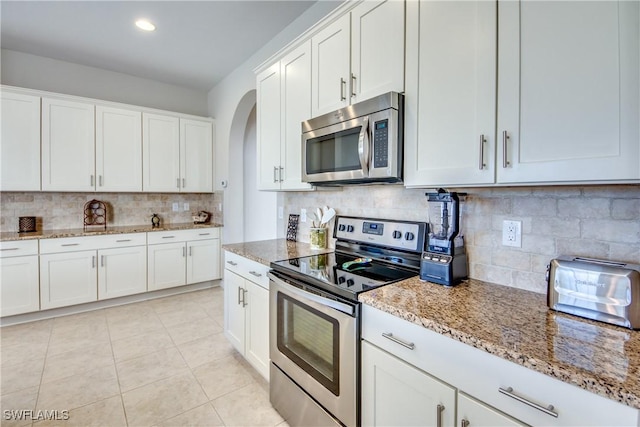 kitchen featuring backsplash, light tile patterned flooring, light stone counters, white cabinetry, and stainless steel appliances