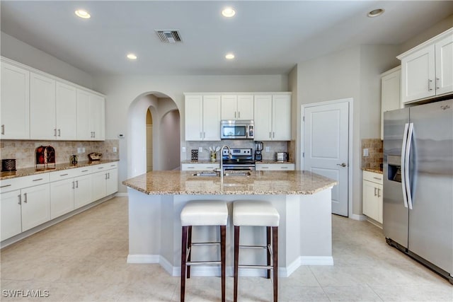 kitchen featuring light stone counters, stainless steel appliances, a kitchen island with sink, sink, and white cabinets