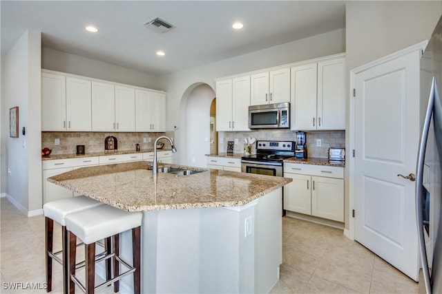 kitchen with light stone countertops, appliances with stainless steel finishes, sink, white cabinetry, and an island with sink