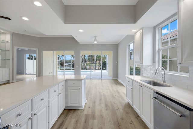 kitchen with decorative backsplash, stainless steel dishwasher, sink, white cabinets, and light hardwood / wood-style floors