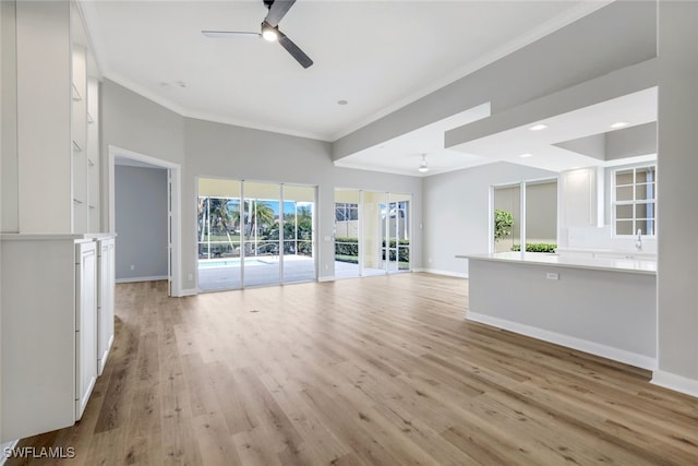 unfurnished living room with ceiling fan, light wood-type flooring, crown molding, and a wealth of natural light