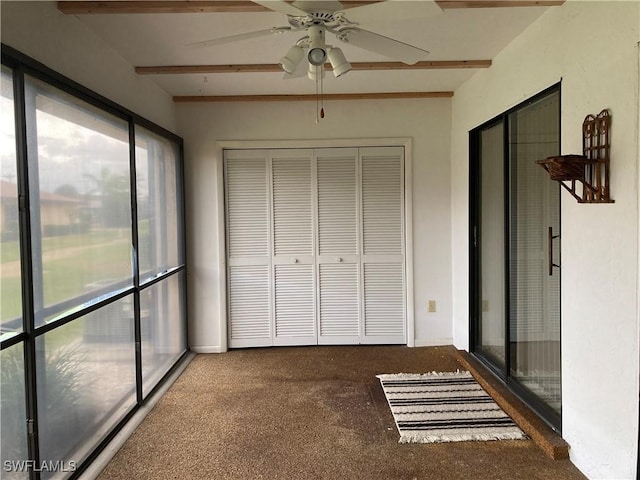 unfurnished sunroom featuring beamed ceiling and ceiling fan