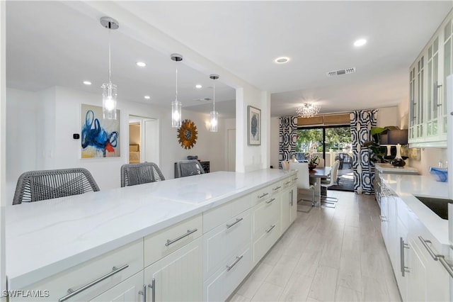 kitchen with light stone countertops, a breakfast bar, white cabinets, light hardwood / wood-style floors, and hanging light fixtures