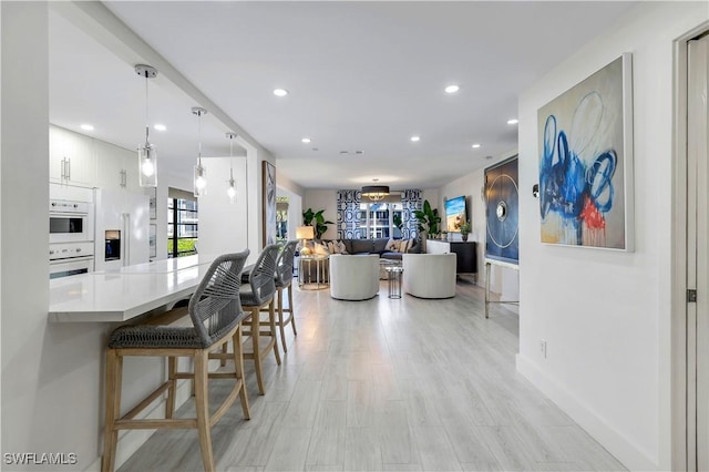 kitchen with a kitchen breakfast bar, light wood-type flooring, white double oven, white cabinetry, and hanging light fixtures