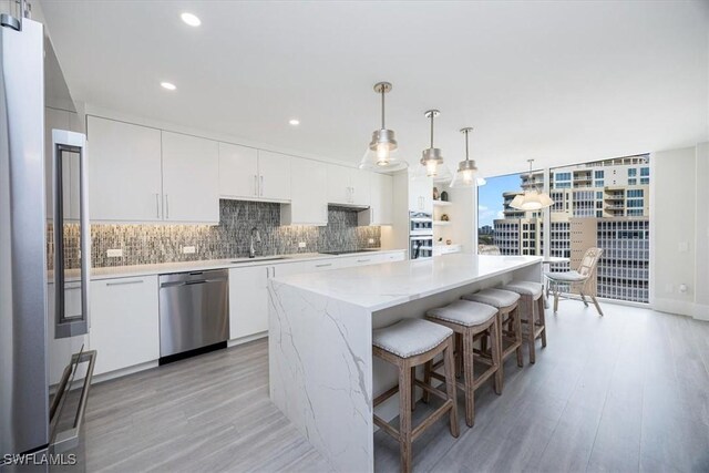 kitchen featuring hanging light fixtures, white cabinets, light hardwood / wood-style floors, a kitchen island, and appliances with stainless steel finishes