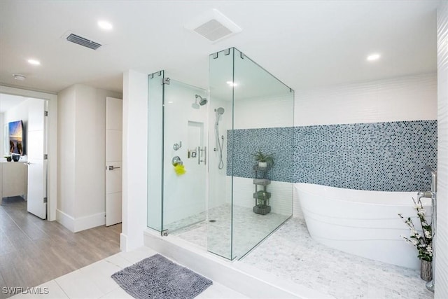 bathroom with hardwood / wood-style floors, tile walls, and independent shower and bath