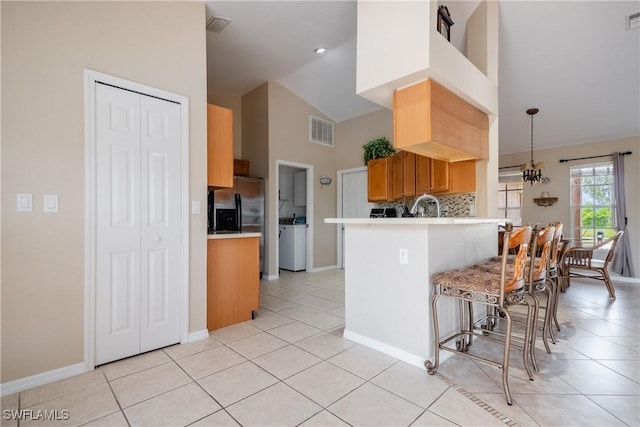 kitchen featuring high vaulted ceiling, light tile patterned floors, decorative light fixtures, kitchen peninsula, and washer / clothes dryer